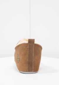 Chausson en daim marron avec une doublure intérieure douce, forme arrondie, couture contrastante et un petit onglet au talon pour un enfilage facile.