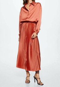 Satin orange bluse med krave, parret med en plisseret midi-nederdel i matchende farve, komplementeret af sorte strophels.