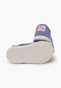 Scarpe di tela azzurro chiaro con suole in gomma bianca, dotate di un'etichetta con una scimmia e la dicitura "Made in Spain" sul tallone. Soletta testurizzata per aderenza.
