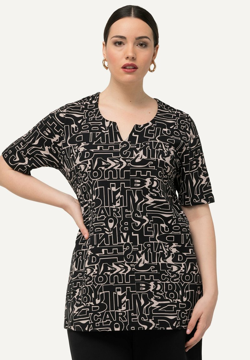 Top de manga corta en negro con letras abstractas en crema. Presenta un escote en V y un corte relajado. Tejido suave con un diseño gráfico impreso.