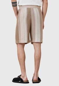 Strickshorts mit gestreiftem Muster in Beige und Creme. Mit geripptem Bund und rohem Saum, aus atmungsaktivem Material gefertigt.