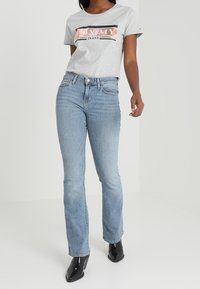 Camiseta gris con el logo "TOMMY JEANS", combinada con unos jeans rectos de color azul claro. Botines negros. Tejido texturizado y ajuste casual.