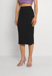 Schwarzer, gerippter Midirock mit hohem Bund und seitlichen Schlitzen, kombiniert mit lila Riemchen-High-Heels. Glatte Textur und taillierte Passform.