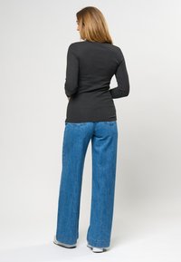 Svart ribbad långärmad tröja kombinerad med vida ljusblå jeans, med en slät yta och en avslappnad passform.