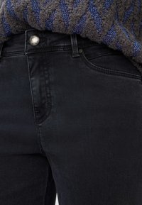 Zwarte denim jeans met een slim fit, met een klassiek zakontwerp en een zilveren knoopdetail in de taille. Het materiaal lijkt glad.