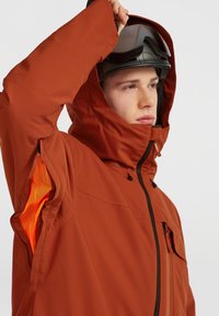 Oranje weerbestendige jas met een ritsluiting, verstelbare capuchon en contrasterende oranje meshvoering in de ventilatieopeningen onder de armen.