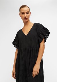 Czarna sukienka z dekoltem w serek, krótkimi falbaniastymi rękawami, textured materiałem i luźnym krojem. Posiada warstwowy krój spódnicy.
