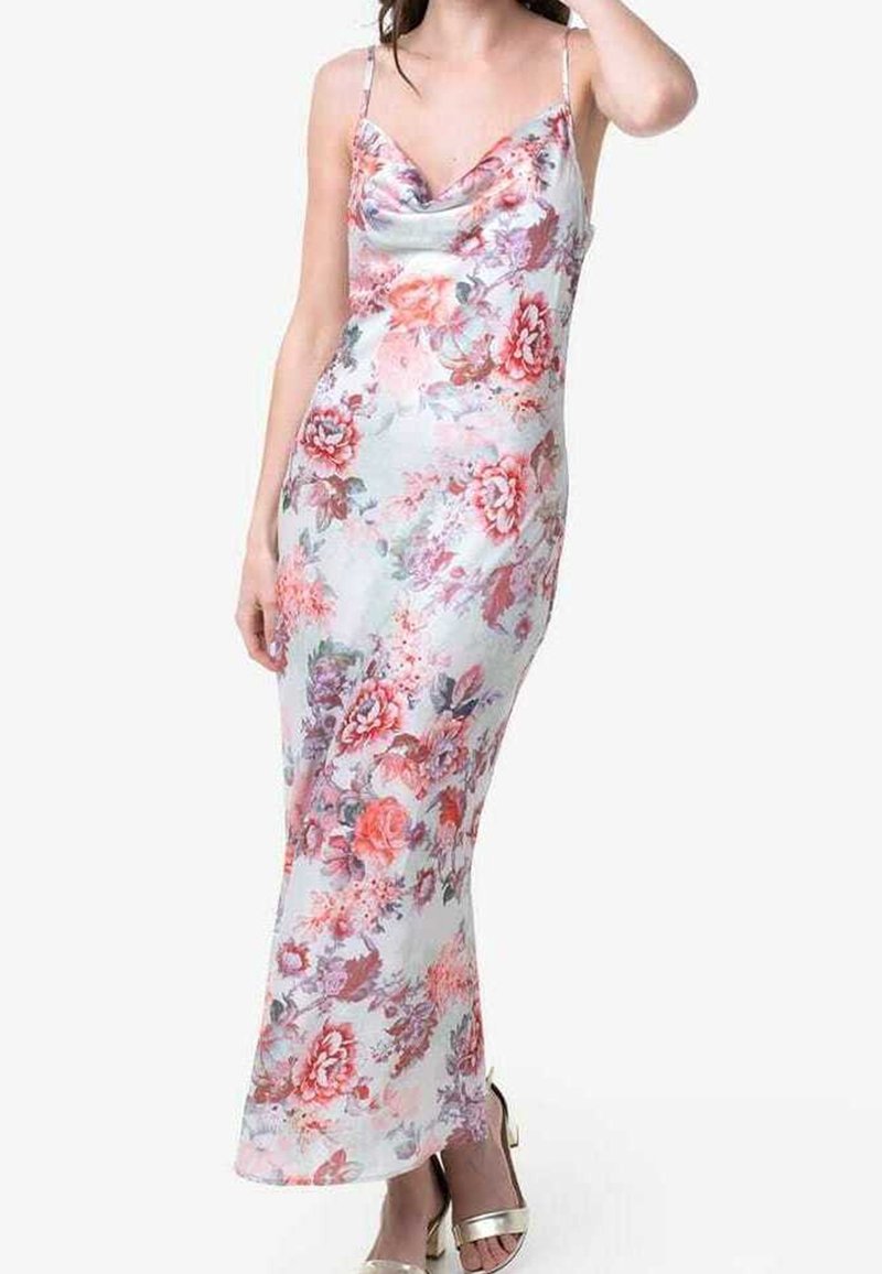 Femme portant une robe longue jusqu'aux chevilles, sans manches, à motifs floraux, avec des bretelles spaghetti et des talons ouverts métalliques, posant avec une main près de sa tête.