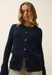 Granatowy sweter dzianinowy o fakturowanym wzorze, z okrągłym dekoltem, zapięciem na guziki i długimi dopasowanymi rękawami.