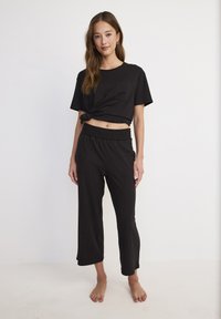 Zwarte korte T-shirt met een voorzak en een geknoopte detail, gecombineerd met loszittende zwarte broek met elastische tailleband en zakken.