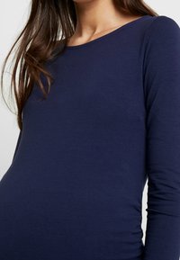 Mörkblå långärmad topp tillverkad av ett mjukt, stretchigt material med rund halsringning och rynkad detalj på sidan, designad för komfort.