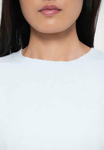 Lyseblå t-shirt med rund hals i blødt stof med en glat tekstur. Har et enkelt design med minimale syninger.