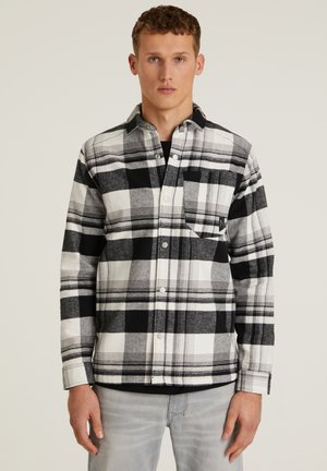 Camisa de franela a cuadros en blanco y negro con cuello abotonado, bolsillo frontal y mangas largas. Textura suave con botones a presión.