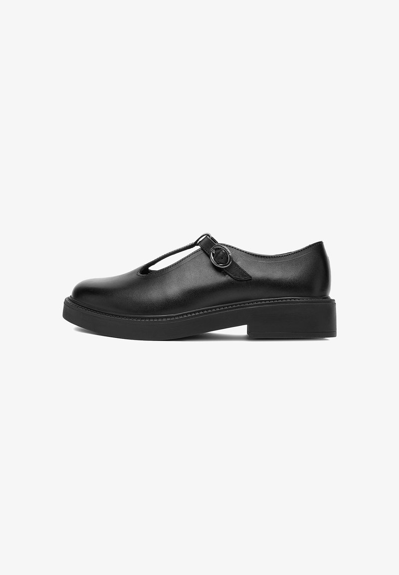 Zapato Mary Jane de cuero negro con punta redondeada, tirante en T, hebilla plateada y suela gruesa de tacón bajo sobre fondo blanco.