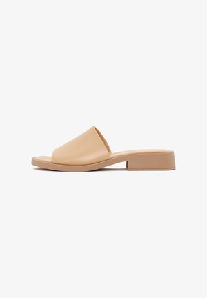 Beige leren instapsandalen met een vlakke, rechthoekige zool en een brede, gladde band die de voorkant van de voet bedekt.