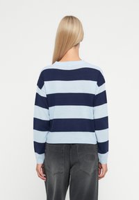 Light blue and navy striped sweater with long sleeves and a round neckline, paired with dark gray pants featuring a logo on the back pocket.