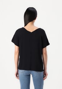 Camiseta negra de cuello en V con mangas cortas, hecha de una tela suave, con un corte relajado y un dobladillo recto, combinada con jeans de color azul claro.