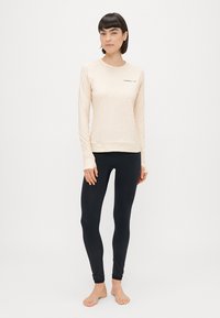 Pikad varrukad koorevalgest topist, millel on peen tekstuur ja logo; mustad retuusid siledast materjalist. Mõlemad on keha lähedal ja mõeldud aktiivseks kasutamiseks.