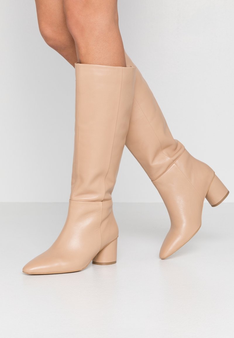 Nude knee-high boots made of smooth leather, featuring a pointed toe and a chunky heel, with a fitted shaft and no visible hardware.