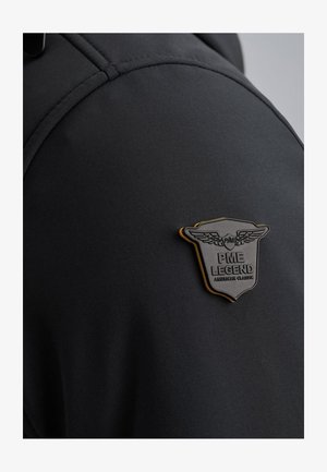 Sort jakke med et tekstureret badge med vinger og teksten "PME LEGEND AMERICAN CLASSIC," der fremhæver dets elegante design og materiale.