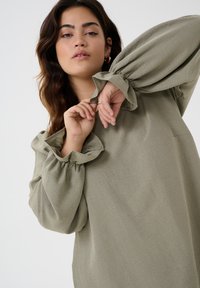 Olive green blouse with voluminous, gathered sleeves. Soft, textured fabric with a relaxed fit. Subtle sheen enhances the overall look.