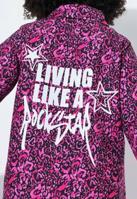 Helle pinke Leopardenmuster-Jacke mit weißem Text "LIVING LIKE A ROCKSTAR" und Stern-Grafiken auf dem Rücken.