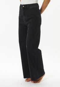 Jeans de mezclilla negros de cintura alta con un ajuste relajado, dobladillo deshilachado y bolsillos frontales. La tela tiene una textura suave y líneas limpias.