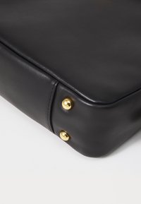 Borsa a tracolla in pelle nera con angoli, caratterizzata da una superficie liscia e dettagli in hardware color oro. Bordo arrotondato con cuciture visibili.