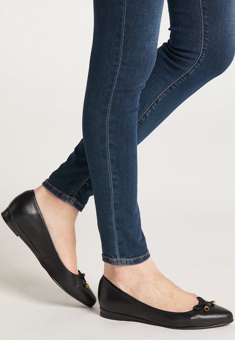 Zwarte platte schoenen met een ronde neus, voorzien van een klein strikje en gouden accenten. Draag ze met donkerblauwe slim-fit jeans. Soepele leren textuur.