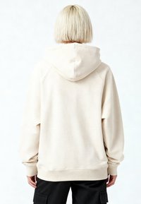 Felpa beige con cappuccio, vestibilità comoda, maniche lunghe e polsini a costine. Il tessuto sembra morbido con una texture spazzolata, vista posteriore mostrata.