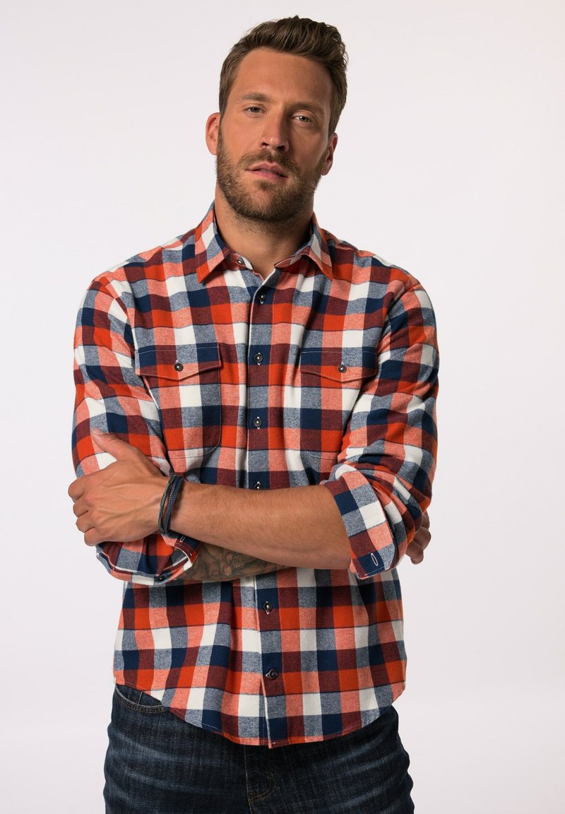 Camisa de campamento en cuadros rojos, azules y blancos; con cuello de botón, dos bolsillos en el pecho y mangas enrolladas. Tejido texturizado con un acabado suave.