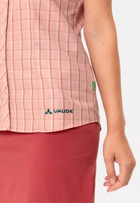 Světle růžová kostkovaná košile s bílými pruhy, krátkými rukávy a zapínáním na knoflíky. Obsahuje zelenou nálepku a tmavě zelené logo "VAUDE".