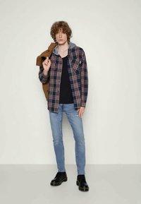 Καρώ πουκάμισο με γκρι κουκούλα, επάνω από μαύρη μπλούζα. Ανοιχτό μπλε τζιν με φθαρμένη λεπτομέρεια. Μαύρες μπότες. Παρουσίαση καθημερινού ντυσίματος.