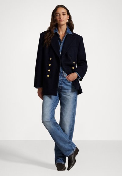 Marineblauer, doppelt geknöpfter Wollblazer mit goldenen Knöpfen, Denimhemd und hellblauen, weit geschnittenen Jeans, kombiniert mit dunklen Stiefeletten.