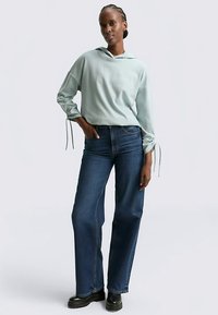 Ljusblå hoodie med dragsko i ärmarna, kombinerad med lösa mörkblå jeans och svarta ankelboots. Mjuk textur, avslappnad passform.