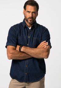 Korte mouwen spijkerblouse in marineblauw, met twee borstzakken en een ronde zoom. De stof heeft een gladde textuur met contrasterende stiksels.
