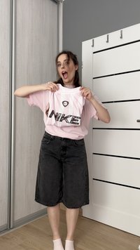 Šviesiai rožinė T-marškiniai su juodu "NIKE" logotipu ir baltu dryžių raštu, derinami su juodais džinsiniais šortais. Savybės: laisvas kirpimas ir apvalus iškirpimas.