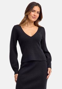 Maglione nero a coste con maniche lunghe e scollatura a V profonda. Tessuto morbido con sottili fibre metalliche. Abbinato a una gonna coordinata.