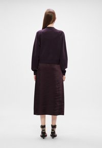 Ljubičasti pleteni pulover s spuštenim ramenima, uparen s dugom, tamnoplava satenskom suknjom i crnim remenima oko članaka s zlatnim detaljima.