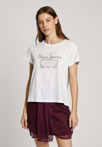 Balta medvilninė T-shirt marškinėliai su apvali apykakle ir trumpomisRankovėmis, dekoruoti išblukusiu pilku grafinio spauda. Sukombinuota su permatomu vyno raudono sijonu.
