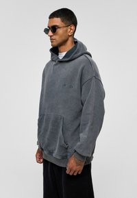 Grijze hoodie met een pluche textuur, oversized pasvorm, kangoeroe-pocket en een trekkoordcapuchon. Bevat subtiele branding en geribde manchetten.