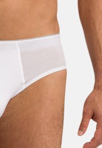 Männlicher Oberkörper und Oberschenkel, die weiße Unterwäsche tragen, mit einer sichtbaren rechten Hand, die entspannt an der Seite liegt.