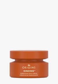 Bol ovale à double couche de couleur orange mat avec une texture lisse. L'étiquette de texte blanche indique "ORIGINS GINZING CRÈME RICHE ÉNERGISANTE."