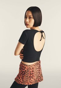 Top nero a maniche corte con un grande taglio sul retro, abbinato a una mini gonna a stampa leopardata arancione e nera. Texture liscia.