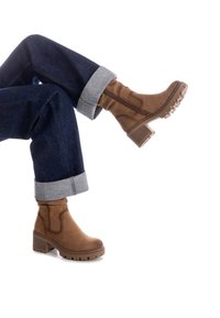Stivali ankle in suede marrone con tacco spesso, zip laterale e suola in gomma, abbinati a jeans scuri con risvoltini.