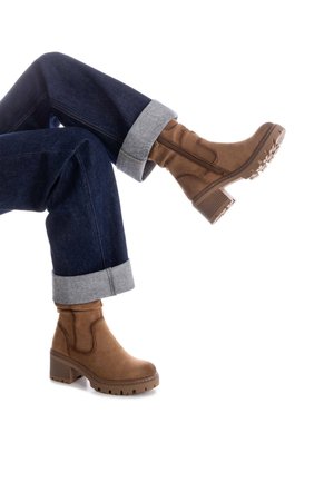 Botas de tobillo de ante marrón con un tacón grueso, cremallera lateral y suela de goma, combinadas con unos jeans oscuros con los puños doblados.