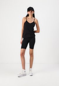 Top nero senza maniche con spalline sottili, abbinato a pantaloni biker neri e scarpe da ginnastica alte bianche. La trama è liscia e elastica.
