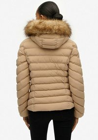 Beige dunjakke med en hætte foret med pels, quiltet design og ribbede detaljer, der viser en glat tekstur og en tætsiddende silhuet.