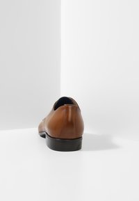 Chaussure en cuir marron avec une texture lisse, de forme arrondie et une semelle en caoutchouc noire. Le talon présente une légère courbe pour un contour.