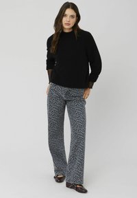 Un pull en tricot noir avec un col montant et des manches longues, associé à un pantalon évasé gris à imprimé léopard et des chaussures plates sombres.